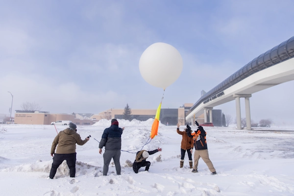 Five people prepare a weather balloon for launch amid a snowy landscape