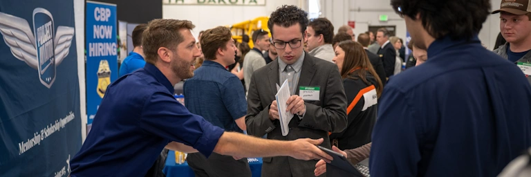 Students speak with recruiters at a career fair in an airport hangar.