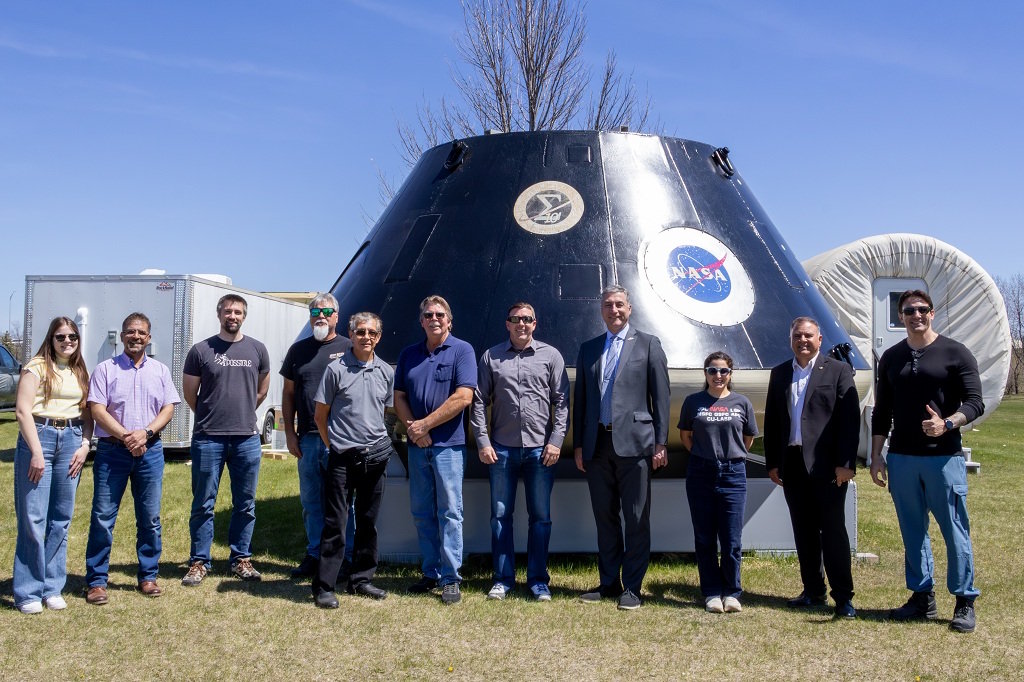 A research group stands in front of a space capsule